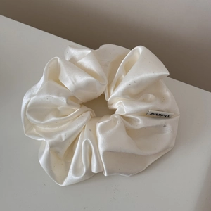 Detail view of cream satin scrunchie with subtle silver sparkles and high-end texture