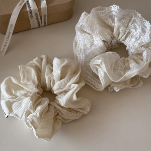 Dettaglio di elastici scrunchie beige in pizzo e fiori accanto a una confezione regalo