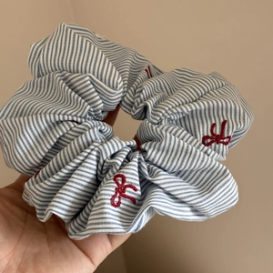 Détail d'un chouchou à rayures bleues avec des nœuds rouges brodés sur le tissu