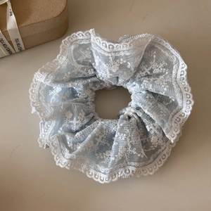 Dettaglio di un elastico in chiffon azzurro con bordi in pizzo e ricami floreali bianchi