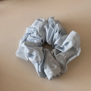 Dettaglio di scrunchie a righe azzurre con ricami floreali bianchi e bordo in pizzo