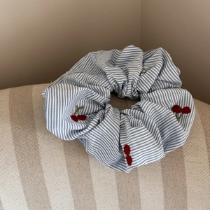 Gros plan sur un chouchou rayé bleu avec broderie cerise rouge et plis de tissu élégants