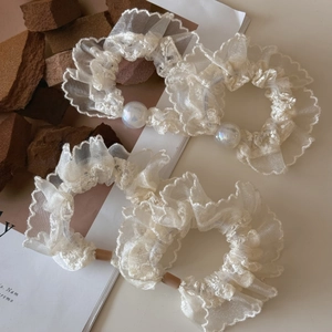 Set of four cream lace organza hair scrunchies with iridescent pearl accents on table
