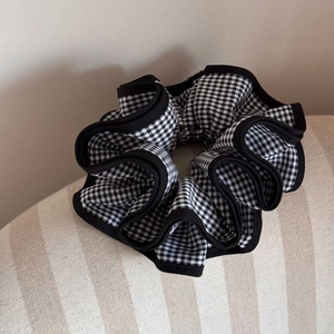 Detail of checkered gingham scrunchie with black ruffled edges on fabric background