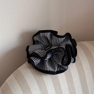 Detail of checkered scrunchie with black ruffled edges on beige textured fabric