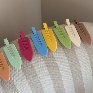Close-up of matte leaf-shaped hair clips in candy colors on beige striped fabric