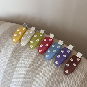 Gros plan de sept barrettes en acrylique coloré avec motifs de marguerites et pinces en métal