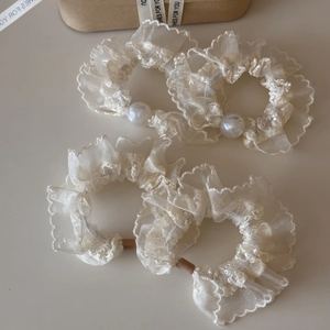 Detailed set of four cream organza scrunchies with pearls and lace on a beige background