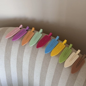 Close-up of ten colorful matte duckbill hair clips arranged neatly on beige fabric