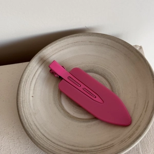 Detail of rose red matte finish hair clip on a minimalist ceramic tray with soft lighting
