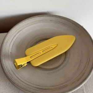Close-up of a matte lemon yellow duckbill hair clip placed on a rustic ceramic plate