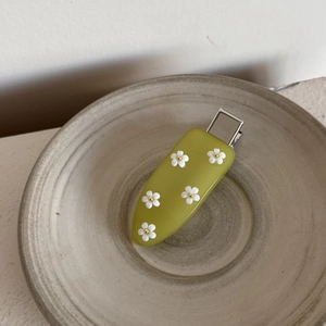 Détail d'une pince à cheveux en acrylique vert avec fleurs 3D dans un bol céramique