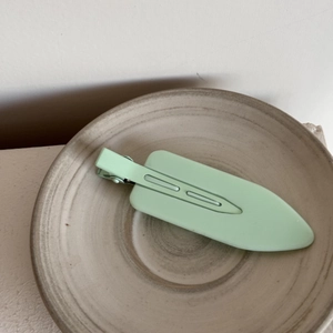 Close-up of a matte mint green hair clip on a textured ceramic plate for daily styling
