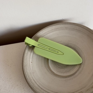 Detail of matte lime green hair clip on a minimalist ceramic plate with natural lighting