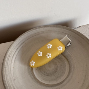 Gros plan d'une pince à cheveux jaune en acrylique avec cinq petites fleurs blanches