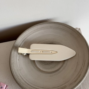 Minimalist matte cream leaf-shaped hair clip on a neutral ceramic tray in a top view