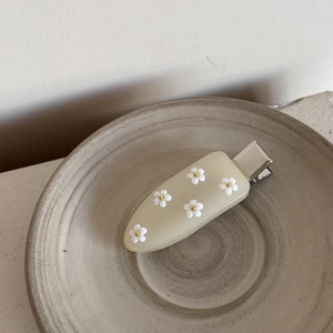 Gros plan d'une pince à cheveux crème avec six fleurs 3D blanches et base métallique argentée