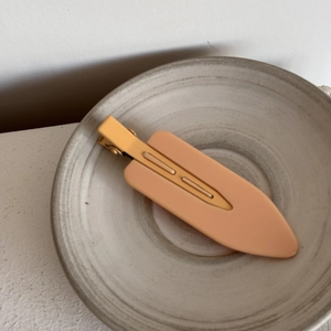 Close-up of matte pink seamless hair clip placed on a minimalist ceramic plate