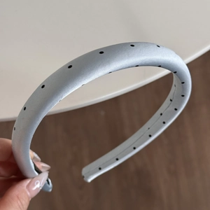 Detail view of a light blue satin polka dot headband with silky smooth texture