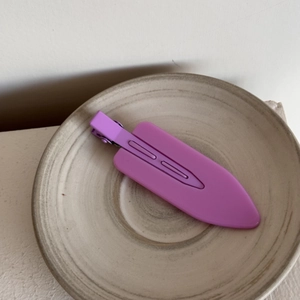 Detail view of a matte purple duckbill hair clip placed in a vintage ceramic tray