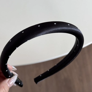 Close-up of a wide padded headband featuring classic black satin with white polka dots