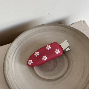 Vue détaillée d'une pince à cheveux rose avec cinq fleurs 3D blanches et cœurs dorés