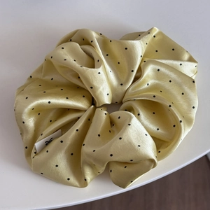 Close-up of yellow silk satin hair scrunchie with black polka dots and woven logo label