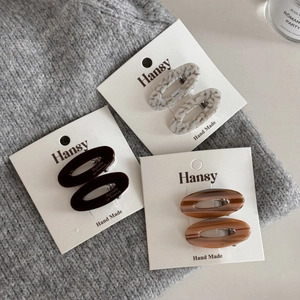 Close-up of three pairs of oval acetate hair clips in assorted textures on a knit base