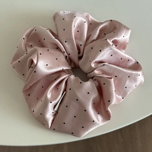 Close-up of pink satin scrunchie with black polka dots and silky pleated texture
