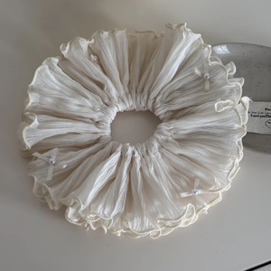 Détail d'un chouchou en mousseline crème avec texture plissée et nœuds en perles