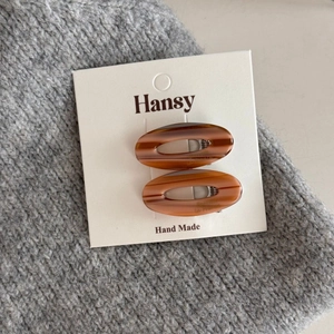Detail view of two oval tortoise shell hair clips on a minimalist white display card