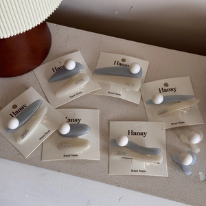 Blue and white pearl ball hair clips on brand cards with a warm aesthetic stone background