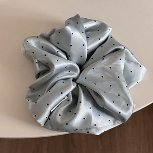 Macro detail of a satin light blue scrunchie with black polka dots and soft texture