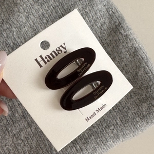 Detail view of dark brown oval acetate hair clips with metallic spring on brand card
