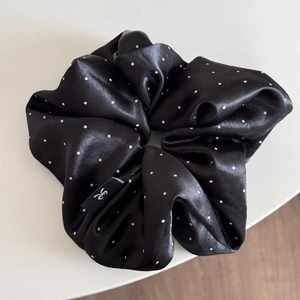 Detailed close-up of a large black satin scrunchie with white polka dots and woven bow label