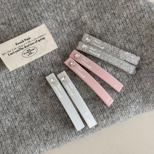 Detailed macro of rhinestone heart hair clips in pink, silver and grey with logo text