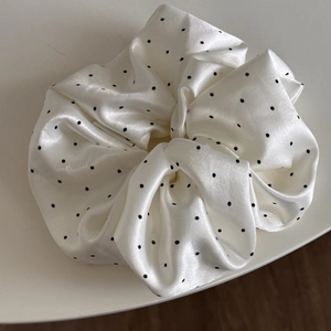 Close-up of white satin scrunchie with black polka dots showing soft pleated fabric texture