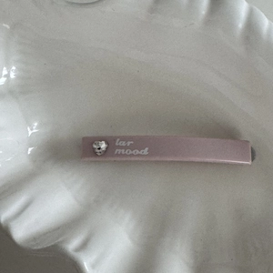 Close-up of dusty pink hair clip with heart rhinestone and artistic white lettering