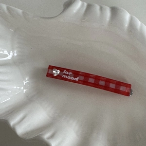 Close-up of red plaid hair clip with heart rhinestone and white text detail