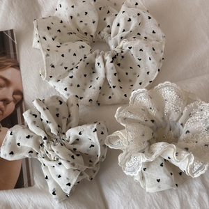 Dettaglio dell'elastico scrunchie bianco con cuori neri ricamati e bordo in pizzo