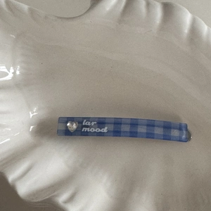 Close-up of blue plaid hair clip with heart rhinestone and white artistic lettering