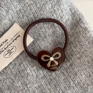 Détail de l'élastique à cheveux marron café avec cœur et nœud sur fond de pull en maille