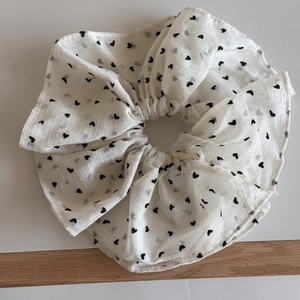 Dettaglio di scrunchie in pizzo bianco con ricamo a cuori neri e motivo a pois