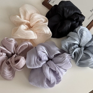 Detail showing various colors of pleated satin hair scrunchies on a minimalist background