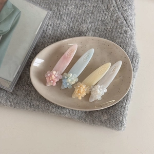 Détail de quatre barrettes à fleurs aux tons pastels avec des perles sur plateau beige