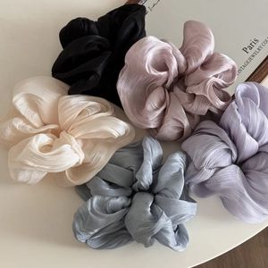 Five glossy pleated satin scrunchies in pastel colors arranged on a minimalist background