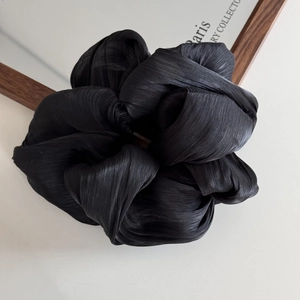 Detailed view of the large black satin scrunchie with soft pleated texture and elegant shine