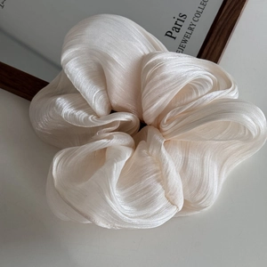Detailed close-up of cream-colored pleated satin scrunchie with subtle pearl luster