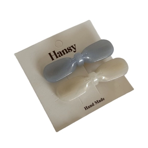 Set of two pearlescent bow hair clips in blue and white on display card for women