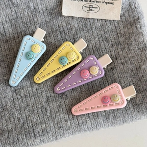 Close-up of four macaron triangle hair clips with smiley faces on a grey background